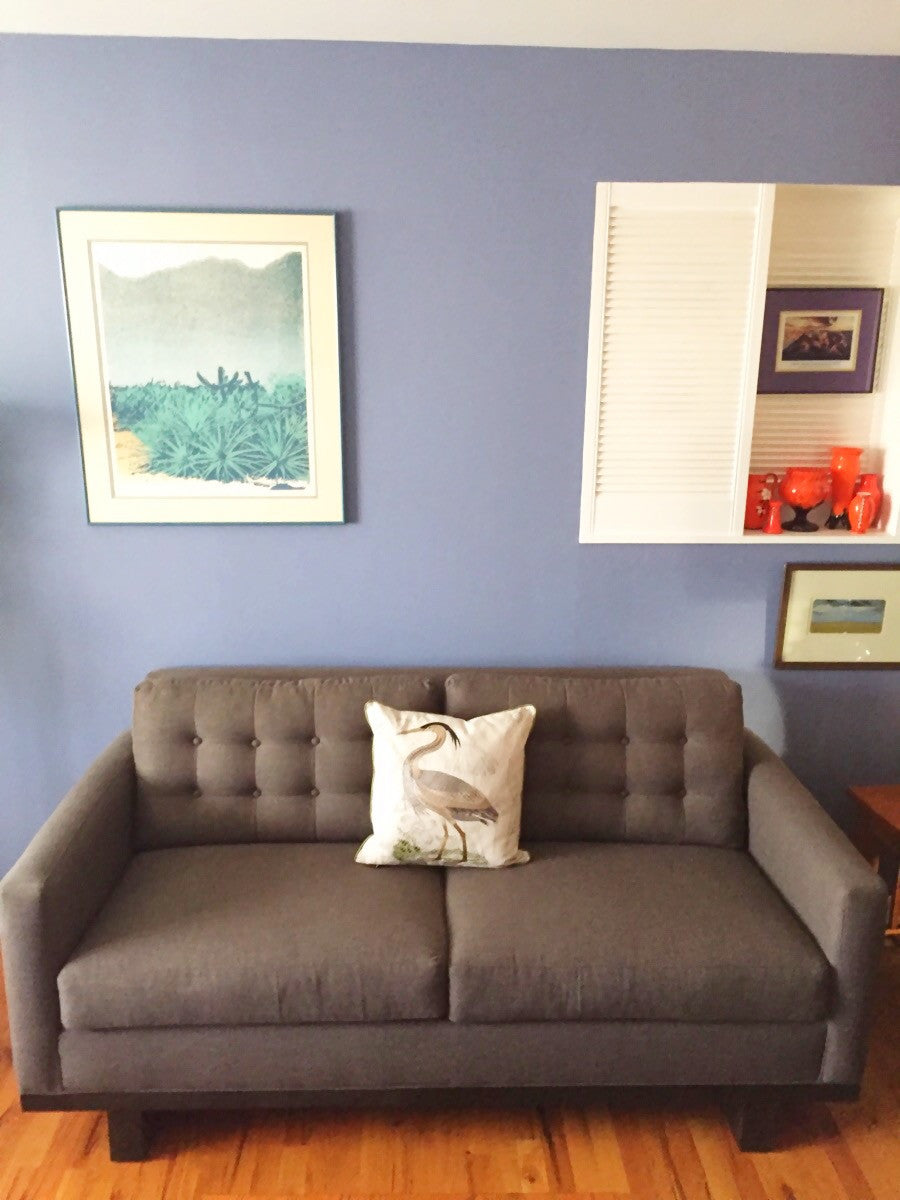 Gray Quinn sofa with one decor pillow and different art prints hanging behind the couch on a wall.