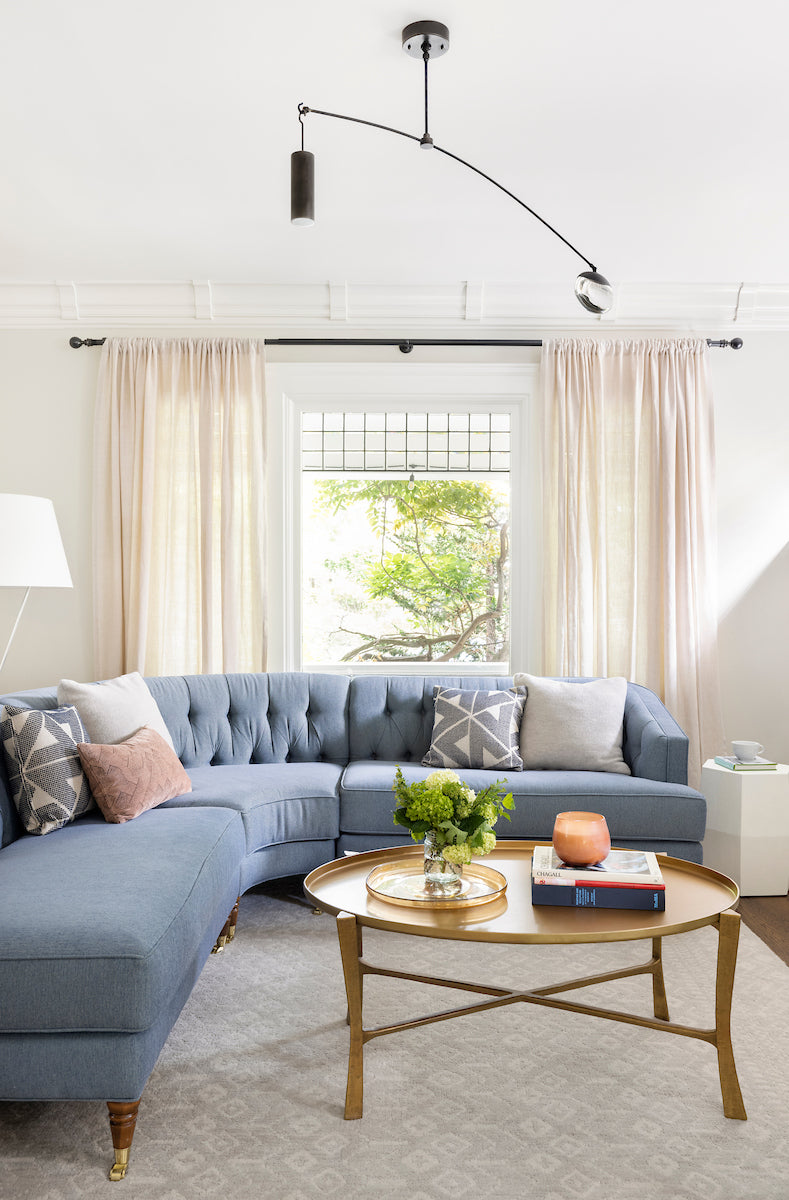 Modern living room with a blue sectional sofa, gold coffee table, and decorative pillows.