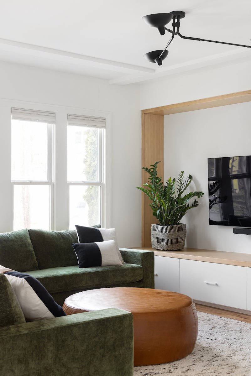 Modern living room with green sofa, wooden coffee table, and TV on a white wall.