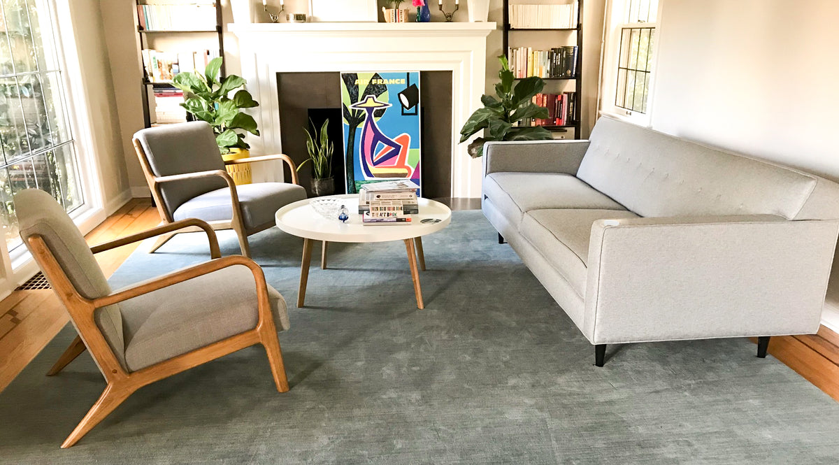 A modern living room with a white modern sofa, two grey chairs with wooden accents and a small white coffee table.